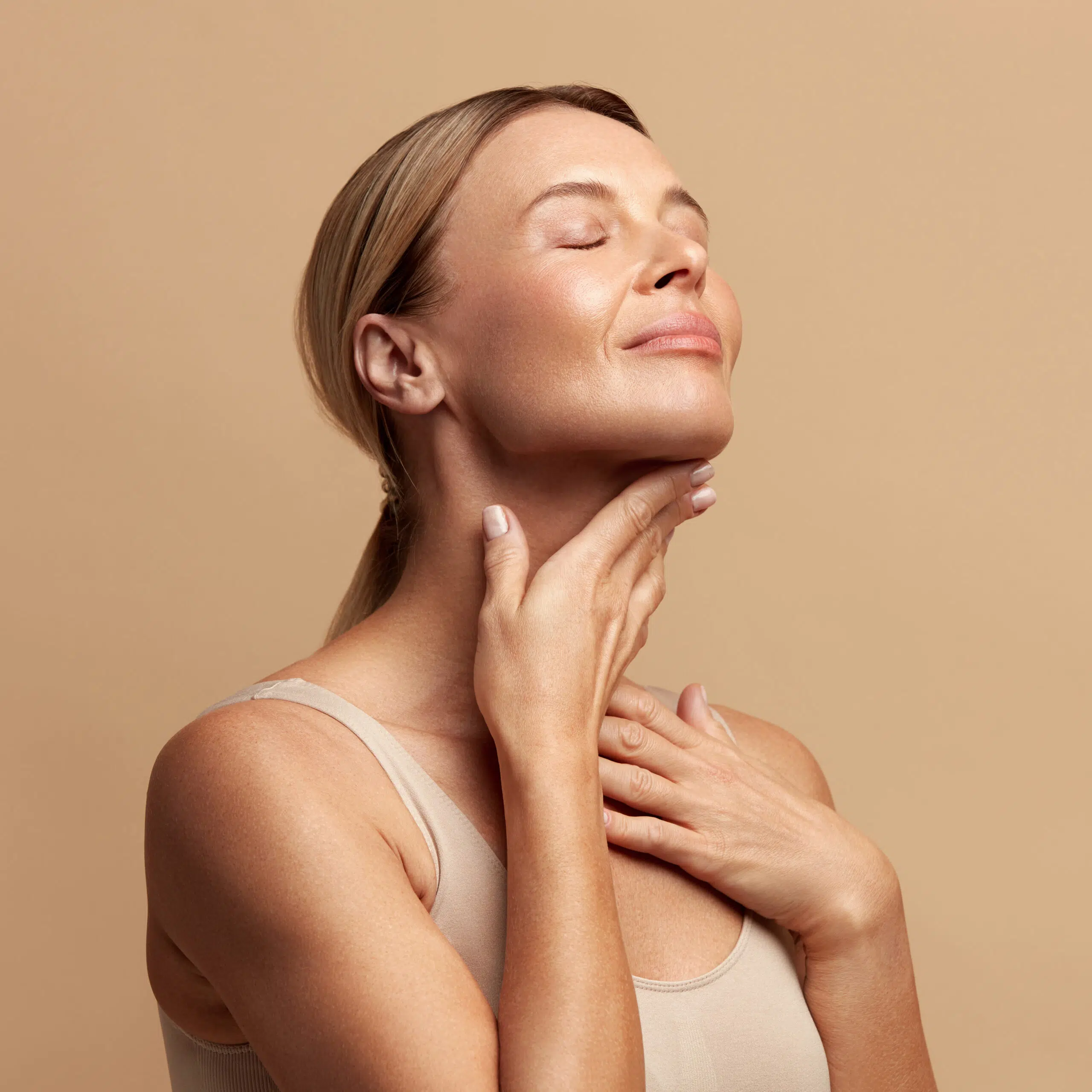 Woman gently touching her neck with eyes closed, displaying healthy skin and a calm, radiant appearance.
