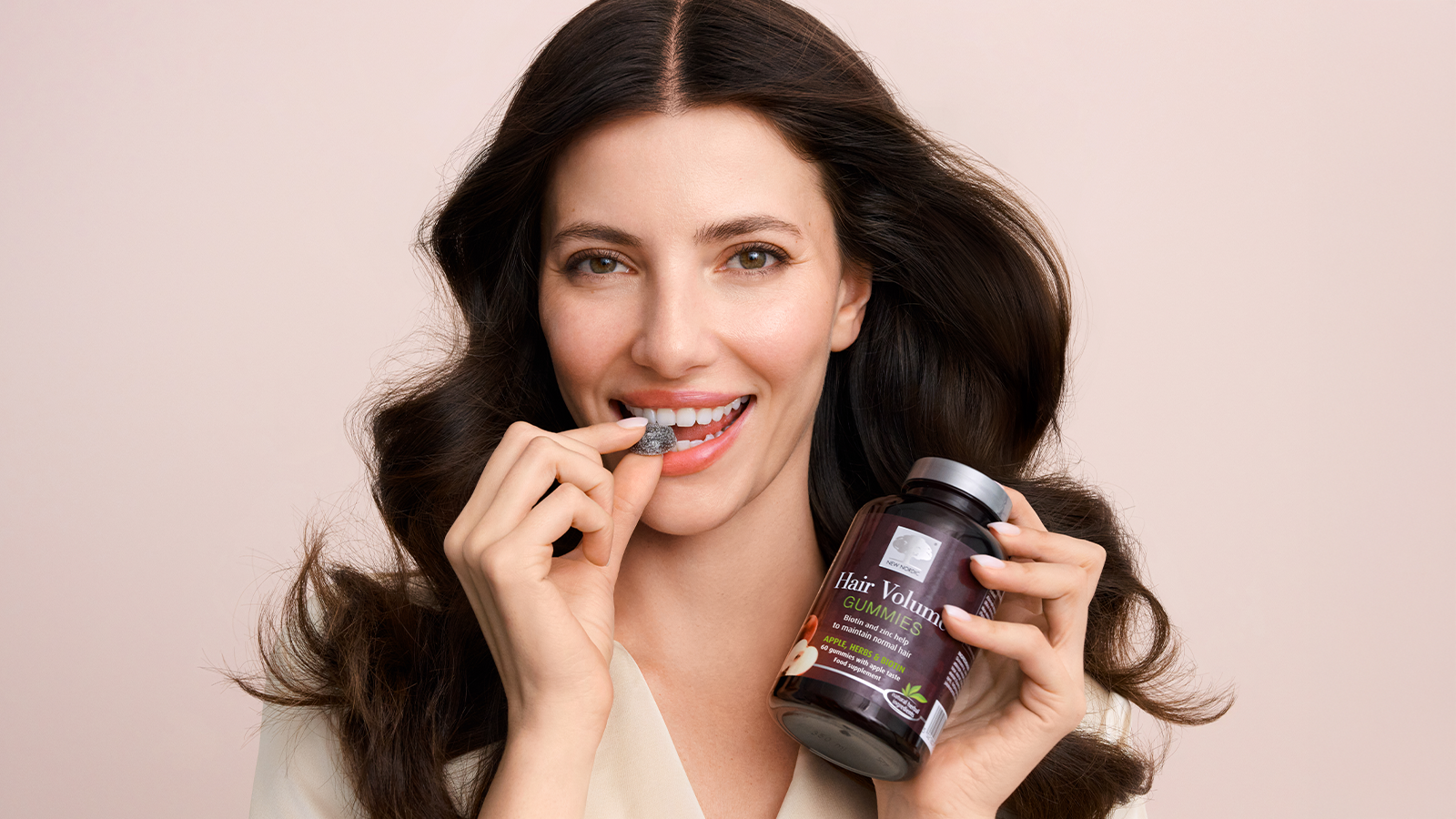 Hair Volume⢠Conditioner 13 A woman holding New Nordic Hair Volume⢠gummies, about to take one in her mouth.